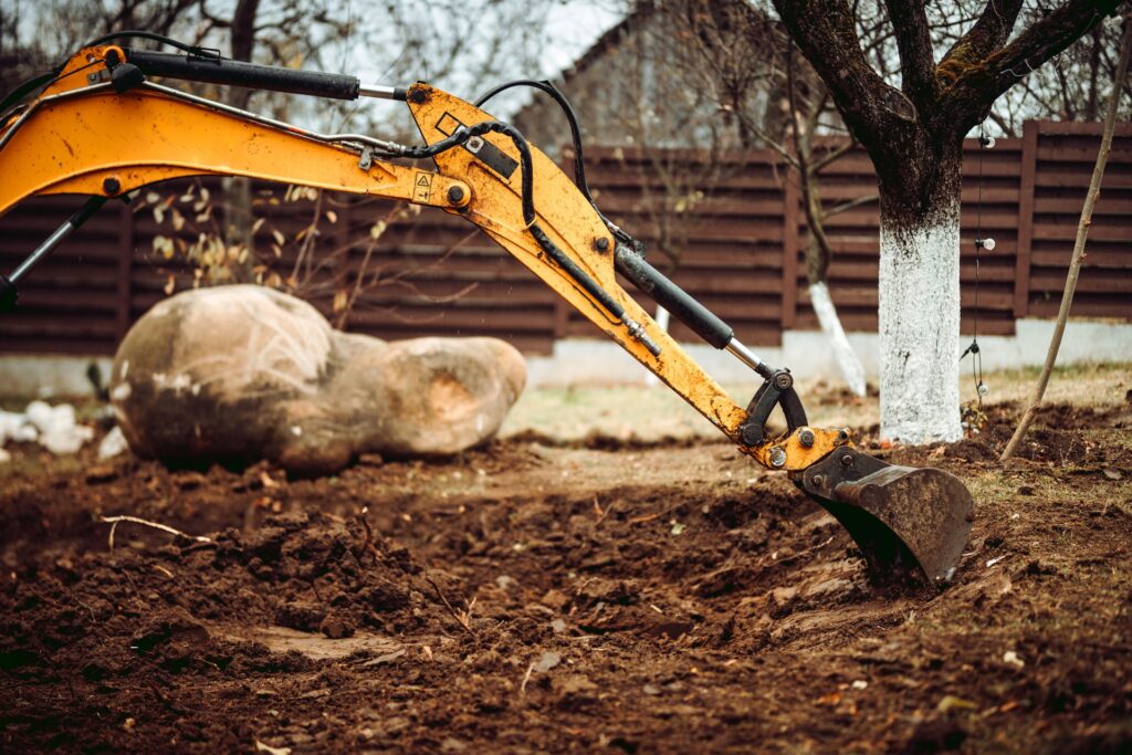 Excavator moving a large boulder in a backyard